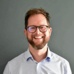 Autism Action CEO Tom Purser. A man in glasses is smiling at the camera against a grey background