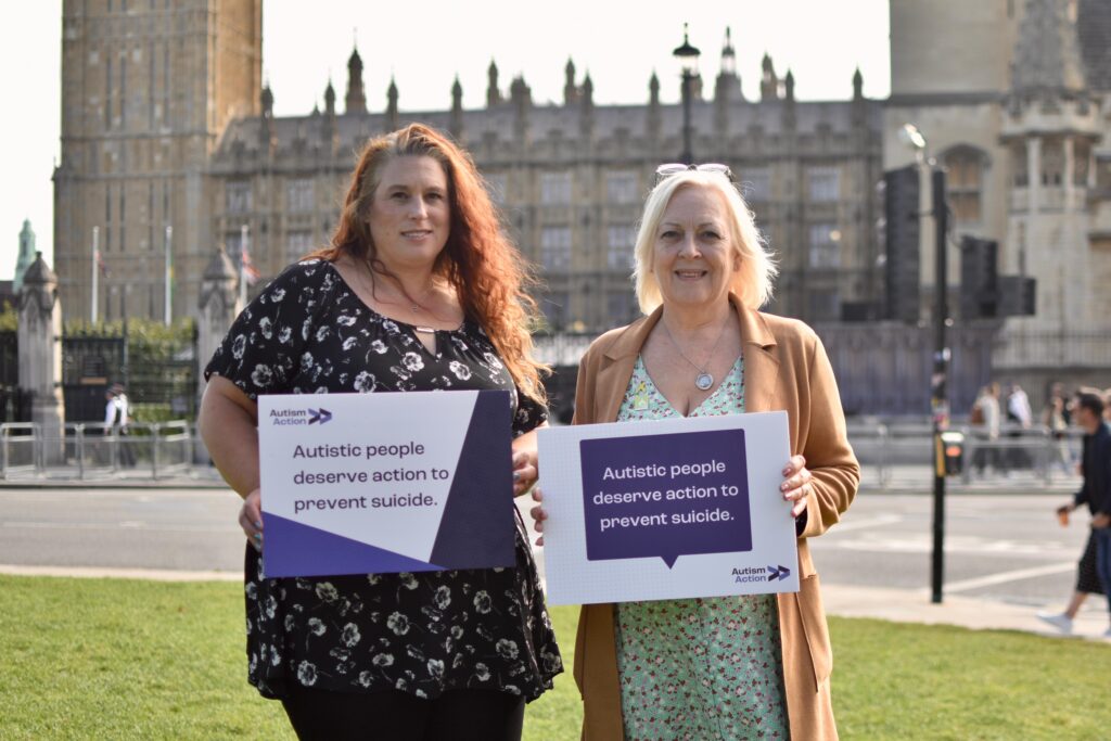 Sharren Bridges and Sue Willgoss stand outside Parliament holding Autism Action banners reading 'Autistic people deserve action to prevent suicide'.